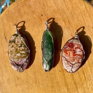 May include: Three wire-wrapped pendants with different types of agate stones. The first pendant features a brown and white agate with a pink and white center. The second pendant features a green agate. The third pendant features a red and white agate.