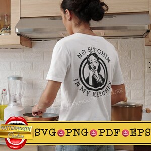 Op de afbeelding: Wit T-shirt met een zwart-witte afbeelding met de tekst "No Bitchin' in My Kitchen". De afbeelding toont een vrouw met een verraste uitdrukking.