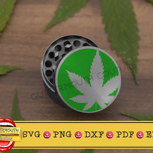 May include: A silver grinder with a green and white marijuana leaf design. The grinder is on a wooden surface with green leaves.