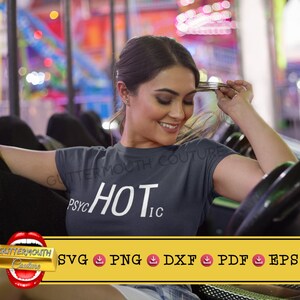 Puede incluir: Una mujer con una camiseta gris con el texto "Psychic Hot" en blanco. Está sentada en un paseo de carnaval.