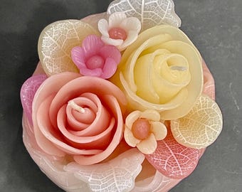 Peut inclure: Bougie en forme de fleurs avec des roses et d'autres fleurs roses, pêche et jaunes. La bougie comprend des détails de feuilles et une base rose clair, créant un objet décoratif et aromatique.