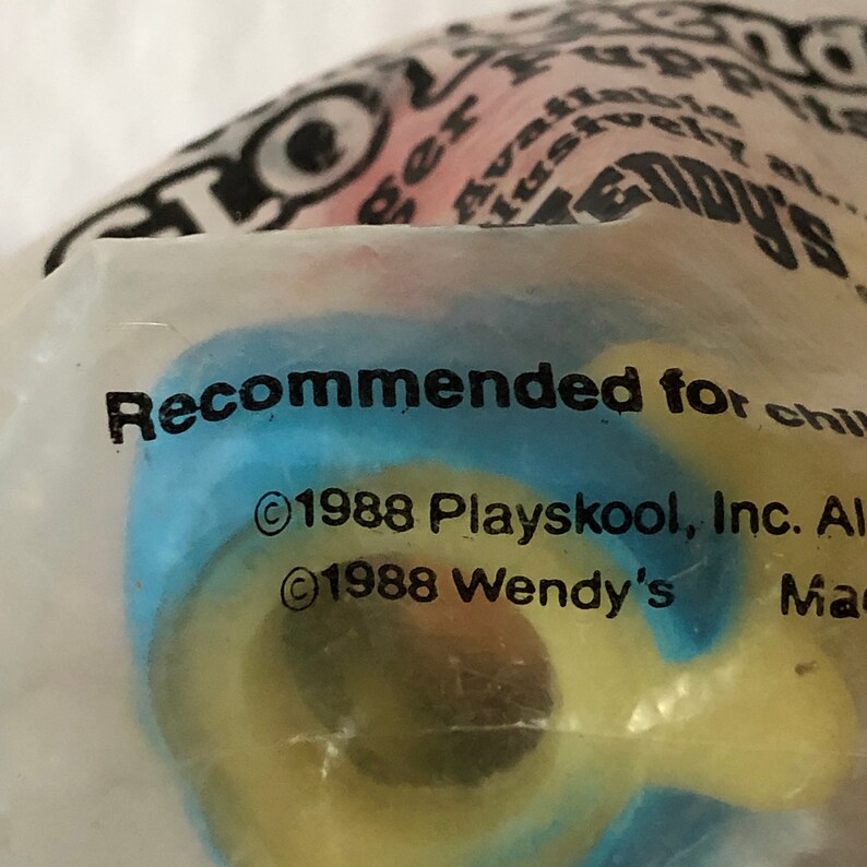 Op de afbeelding: Een close-up van een blauw, geel en rood speelgoed met de tekst "Aanbevolen voor kinderen" en "&copy;1988 Playskool, Inc. Alle rechten voorbehouden" en "&copy;1988 Wendy's"