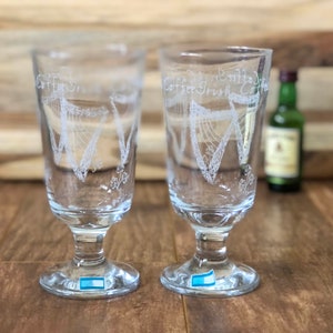 May include: Two clear glass coffee glasses with a harp and shamrock design. The glasses have the words "Coffee Irish" etched on them.