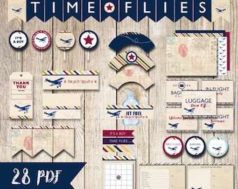 Puede incluir: Un conjunto de decoraciones para fiestas con temática de aviación, que incluye pancartas, adornos para cupcakes y etiquetas. El diseño presenta un motivo de avión vintage con una paleta de colores azul marino, rojo y beige. El texto incluye "TIME FLIES" y "IT'S A BOY".