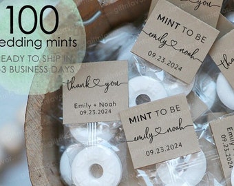 May include: A close-up of 100 wedding mints in clear cellophane bags with personalized brown paper tags. The tags have the text "Mint to be" with the couple's names and wedding date. The mints are round and white.