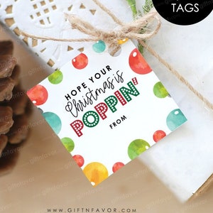 May include: A white square gift tag with a colorful watercolor background of red, green, blue, and yellow circles. The text on the tag reads "Hope your Christmas is POPPIN' from".