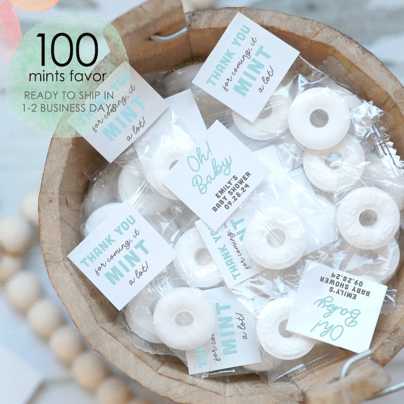 May include: A wooden bowl filled with individually wrapped mint candies. Each candy is round with a hole in the center. Small square tags with the text "Thank you for coming, it MINT a lot!" and "Oh! Baby" are attached to the candies.
