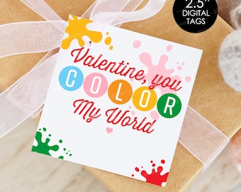 Op de afbeelding: Een wit cadeaulabel met de tekst "Valentine, you COLOR My World" in het rood, met kleurrijke verfspatten. Het label is 6,35 cm in diameter en ligt op een ingepakt cadeau met een wit lint.
