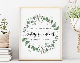 May include: A white sign with a gold frame, featuring a green eucalyptus wreath with the text "PLEASE TAKE HOME A baby succulent & WATCH IT GROW!"