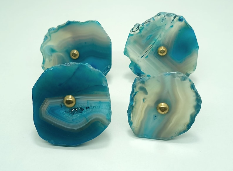 May include: Four agate drawer pulls with a blue and white pattern and gold accents. The pulls are shaped like a natural agate stone.