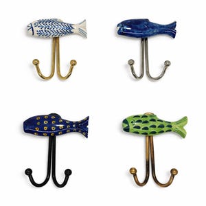 Op de afbeelding: Vier decoratieve wandhaken met visvormige keramische toppen. De vissen zijn blauw, groen en wit, met gouden, zilveren en zwarte metalen haken. De haken zijn ontworpen om items op te hangen.