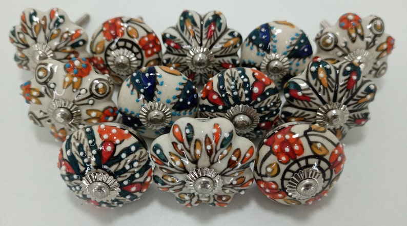 May include: A collection of 12 ceramic drawer knobs with a white base and colorful floral patterns. The knobs have a silver metal base and are perfect for adding a touch of vintage charm to any home.
