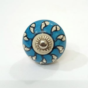 Op de afbeelding: Een blauwe keramische knop met een wit en zwart bloemenontwerp. De knop heeft een zilveren midden.