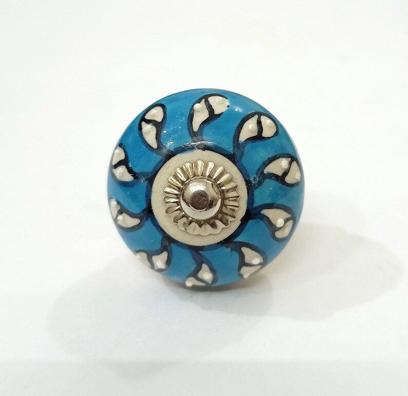 Op de afbeelding: Een blauwe keramische knop met een wit en zwart bloemenontwerp. De knop heeft een zilveren midden.