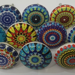 Może przedstawiać: Dziesięć kolorowych ceramicznych gałek do szafek z misternymi wzorami mandali. Każda gałka ma inną kombinację kolor&oacute;w i wz&oacute;r, w tym niebieski, zielony, czerwony, ż&oacute;łty i czarny.