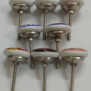 May include: Set of seven ceramic cabinet knobs with colourful floral designs. Each knob has a silver base and a threaded screw.