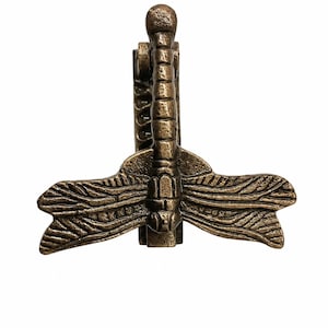 Puede incluir: Un pasador de corbata de metal en tono bronce con un dise&ntilde;o detallado de lib&eacute;lula. El insecto tiene un cuerpo segmentado y alas texturizadas que se extienden horizontalmente. El mecanismo de clip es visible detr&aacute;s de la lib&eacute;lula.