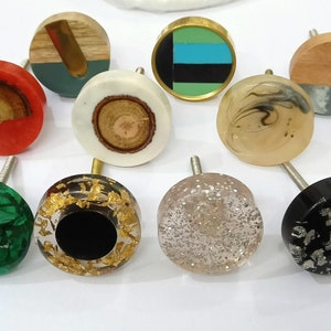 May include: Assortment of 10 decorative round cabinet knobs with various designs and colors. The knobs feature a variety of materials, including wood, resin, and metal. Some knobs have a glittery finish, while others have a smooth, polished surface.