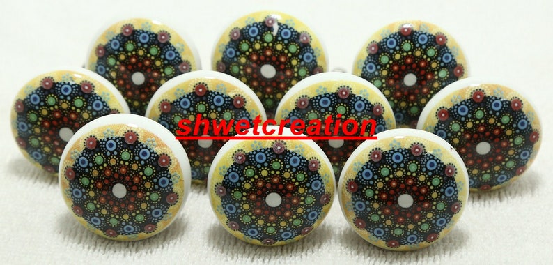 May include: Nine round ceramic knobs with a yellow background and a colourful mandala design. The mandala features a black centre with concentric circles of red, blue, green, and yellow dots.