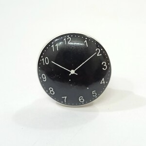 May include: Black and white clock face with white numbers and hands on a black background. The clock face is round and has a white border.