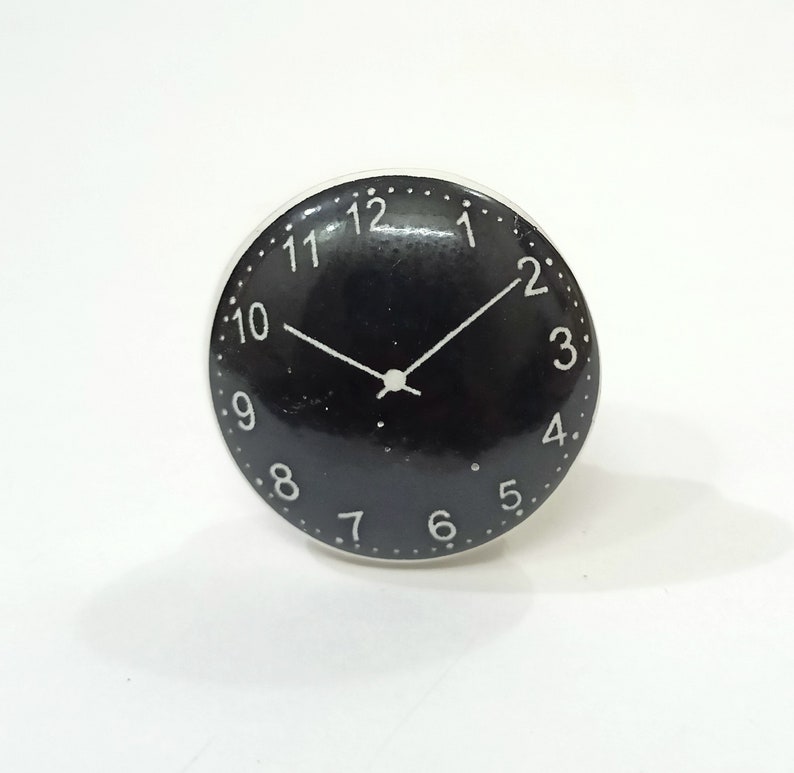 May include: Black and white clock face with white numbers and hands on a black background. The clock face is round and has a white border.