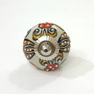 Op de afbeelding: Witte keramische knop met een bloemenmotief in tinten oranje, geel en zwart. De knop heeft een zilveren metalen basis.
