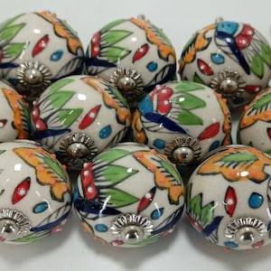 K&ouml;nnte beinhalten: Zw&ouml;lf Keramik-Kn&ouml;pfe mit wei&szlig;em Hintergrund und bunten Blumenmustern. Die Kn&ouml;pfe haben eine silberne Metallbasis.