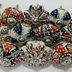 May include: A set of 12 ceramic cabinet knobs with a white base and colorful floral designs. The knobs have a silver finish and a screw for installation.