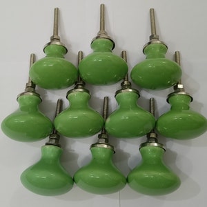May include: Ten green ceramic cabinet knobs with silver metal stems. The knobs are round and have a slightly bulbous shape.