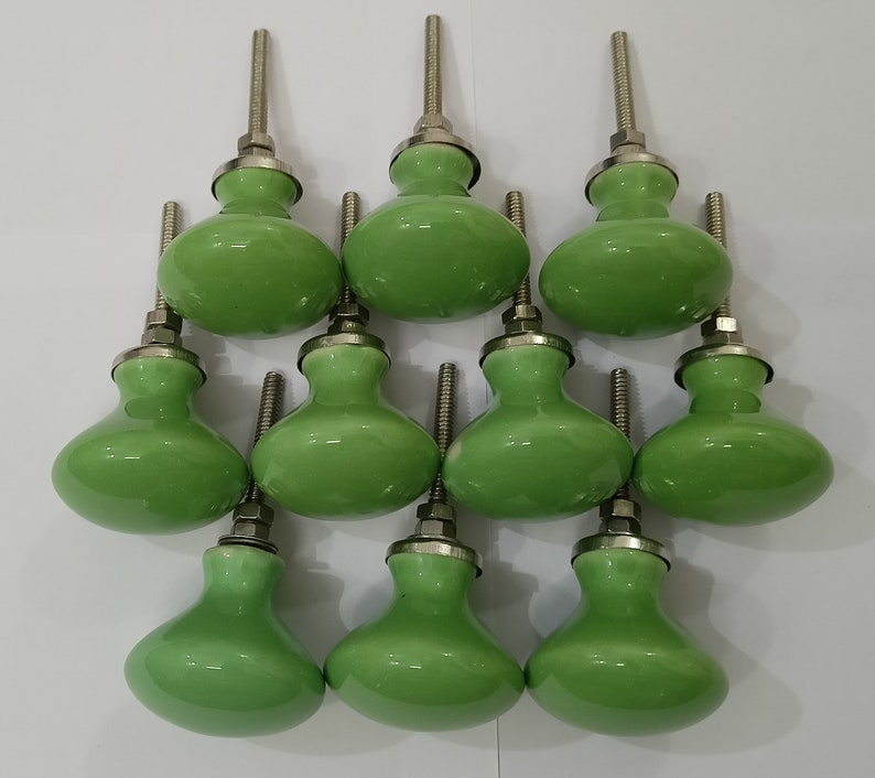May include: Ten green ceramic cabinet knobs with silver metal stems. The knobs are round and have a slightly bulbous shape.