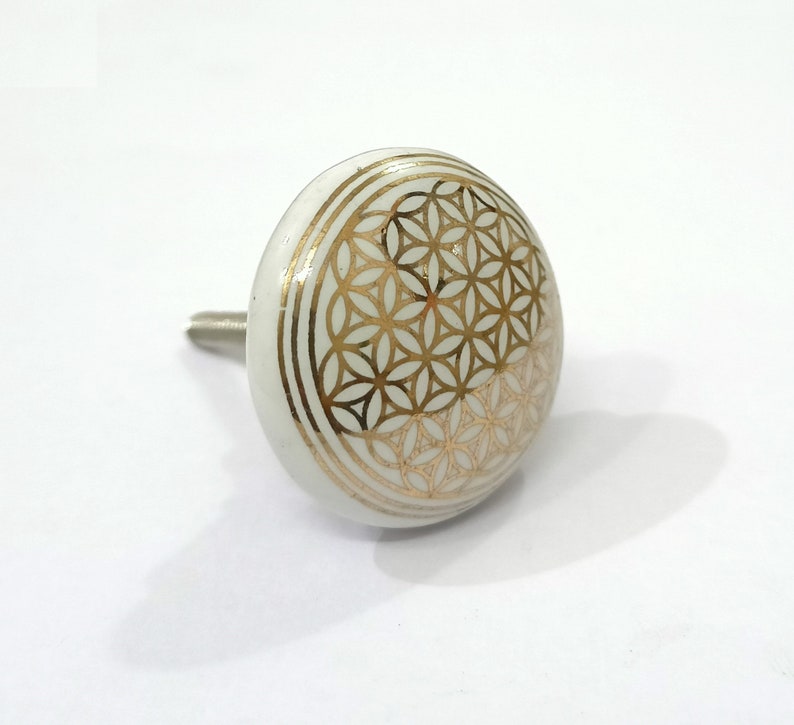 May include: White ceramic cabinet knob with a gold geometric pattern. The pattern is a flower of life design.