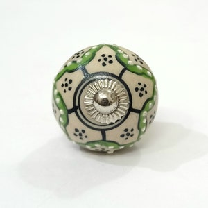 Op de afbeelding: Een witte keramische knop met een geometrisch patroon in groen en zwart. De knop heeft een zilveren metalen midden.