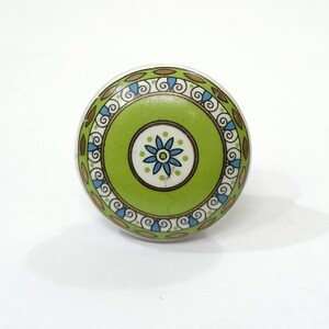 May include: A green ceramic knob with a white and gold floral design. The knob has a decorative border with swirls and leaves.