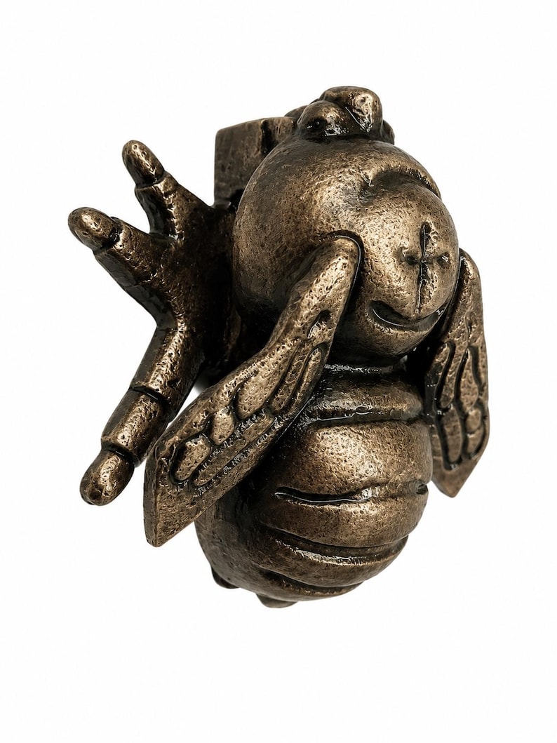 Puede incluir: Un llamador de puerta de metal en tono bronce con forma de abeja. El insecto presenta una cabeza redondeada con una marca en forma de cruz, un cuerpo segmentado y alas texturizadas extendidas hacia los lados. Incluye un mecanismo articulado.
