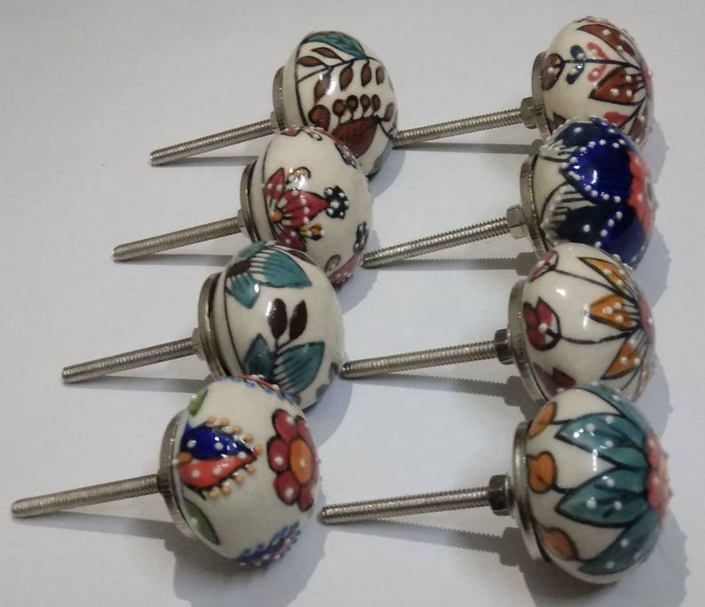 May include: Set of 8 ceramic cabinet knobs with colorful floral patterns. Each knob has a silver metal screw. The knobs are white with blue, red, green, and brown accents.