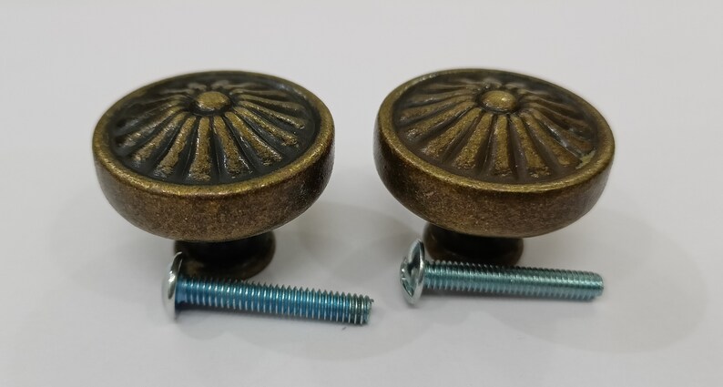 Pu&ograve; includere: Due pomelli per armadi in oro antico con un design a raggiera decorativo e viti abbinate.