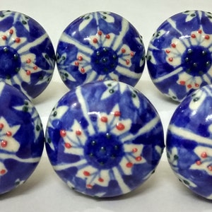 Op de afbeelding: Zes blauwe en witte keramische knoppen met een bloemenpatroon. De knoppen hebben een witte achtergrond met blauwe en rode bloemenpatronen.