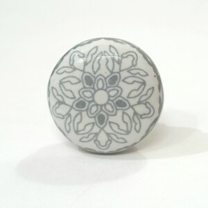 May include: White ceramic knob with a grey floral design.