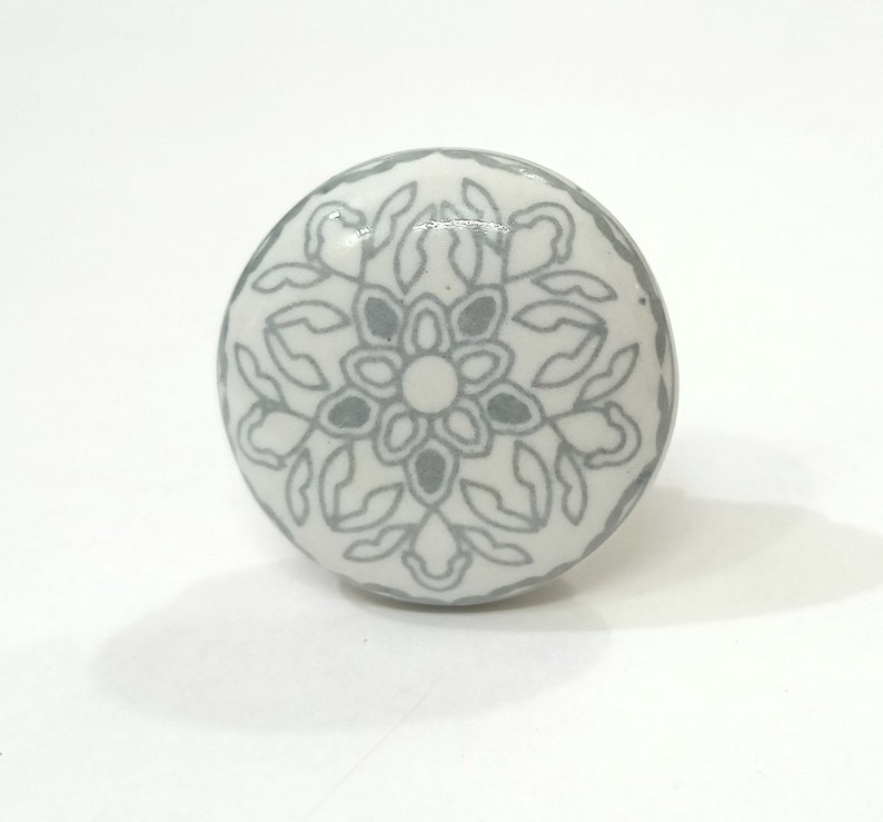 May include: White ceramic knob with a grey floral design.