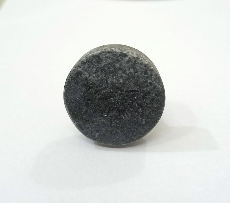 K&ouml;nnte beinhalten: Ein dunkelgraues, zylindrisches Objekt mit strukturierter Oberfl&auml;che. Das Objekt scheint aus Stein oder einem &auml;hnlichen Material zu bestehen. Die Form ist abgerundet, mit flacher Ober- und Unterseite. Das Objekt befindet sich vor einem wei&szlig;en Hintergrund.