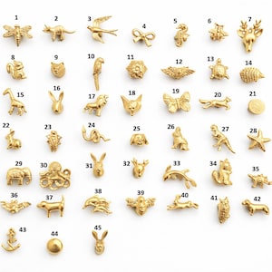 Pode incluir: Uma coleção de pequenos pingentes de metal dourado em várias formas de animais e objetos. Os pingentes incluem uma libélula, um dinossauro, um pássaro, um laço, um cavalo-marinho, uma abelha, um veado, um esquilo, um coelho e mais.