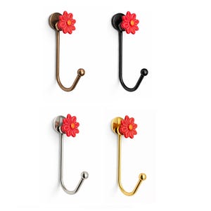 Puede incluir: Cuatro percheros de pared decorativos con un diseño de flor roja. Los ganchos están disponibles en diferentes acabados metálicos: latón, negro, plata y oro. Cada gancho tiene un diseño curvo con una pequeña bola en el extremo.