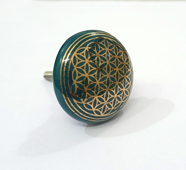 May include: A teal blue ceramic cabinet knob with a gold flower of life design.