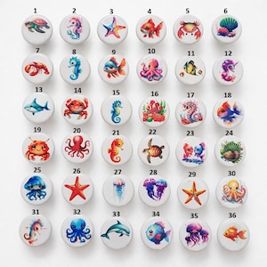 Peut inclure: Ensemble de 36 boutons de placard ronds avec des motifs de créatures marines. Chaque bouton présente une illustration colorée différente de la vie marine, notamment des tortues, des hippocampes, des étoiles de mer, des poissons, des crabes et des méduses. Les boutons sont blancs et brillants.