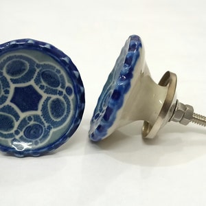 Może przedstawiać: Dwa ceramiczne gałki drzwiowe z niebiesko-białym wzorem. Jeden gałka jest pokazany z boku, ukazując srebrną śrubę i metalową podstawę. Drugi gałka jest pokazany z przodu, prezentując skomplikowany wz&oacute;r.
