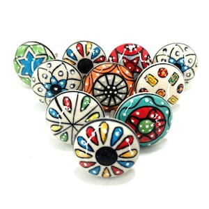 Könnte beinhalten: Eine Sammlung dekorativer Keramik-Schrankknöpfe. Jeder Knopf hat ein einzigartiges handgemaltes Design mit leuchtenden Farben wie Blau, Rot, Gelb und Grün. Die Knöpfe sind rund und haben eine schwarze Mitte, ideal zum Aufpeppen von Möbeln.