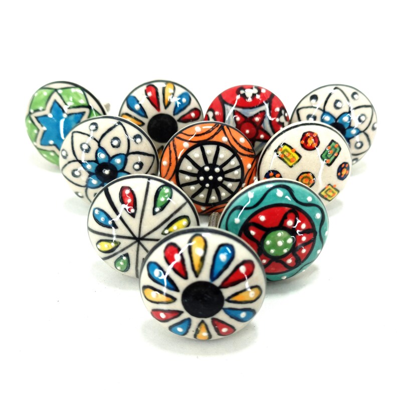 Op de afbeelding: Een verzameling decoratieve keramische kastknoppen. Elke knop heeft een uniek handgeschilderd ontwerp met levendige kleuren zoals blauw, rood, geel en groen. De knoppen zijn rond en hebben een zwart midden, perfect om meubels op te fleuren.