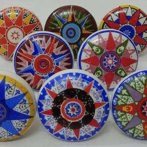 May include: Eight ceramic knobs with a starburst design in various colours, including red, blue, yellow, green, and purple. Each knob features a unique pattern within the starburst.