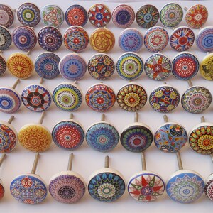 Pu&ograve; includere: Una collezione di 40 pomelli per armadi in ceramica colorati con intricati disegni di mandala. Ogni pomello presenta un motivo e una combinazione di colori diversi, tra cui rosso, blu, giallo, verde e bianco.