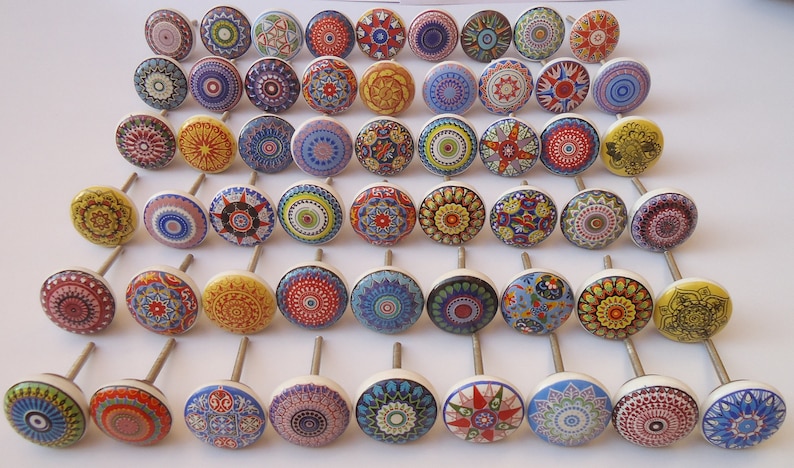 Pu&ograve; includere: Una collezione di 40 pomelli per armadi in ceramica colorati con intricati disegni di mandala. Ogni pomello presenta un motivo e una combinazione di colori diversi, tra cui rosso, blu, giallo, verde e bianco.